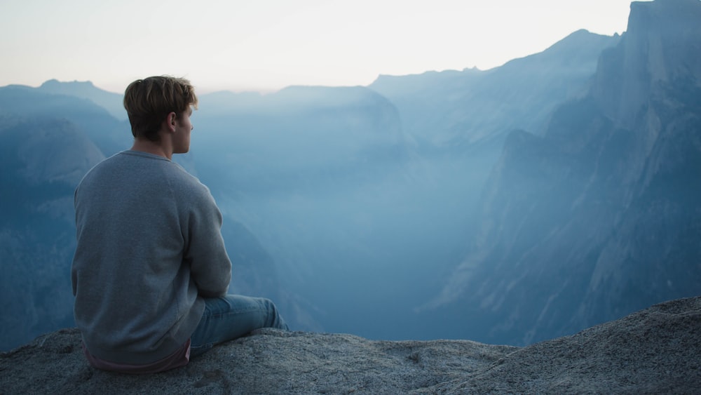 Man practicing mindfulness on a mountain cliff.