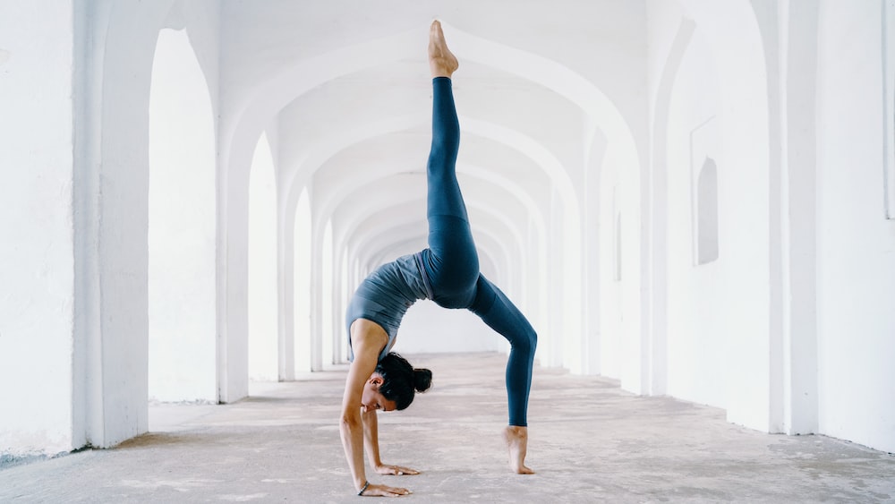 Mindful Yoga: Yogini in Blue Leggings Doing Backbend Pose in White Archway