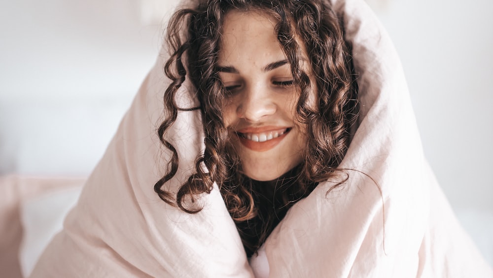 Self-improvement morning vibes: Embrace growth with a smiling woman wrapped in a gray blanket
